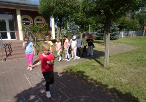 dzieci bawią się o ogrodzie przedszkolnym w piękny słoneczny dzień, grają w klasę reszta grzecznie czeka na swoją kolej